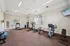 Bright and spacious fitness room with modern exercise equipment including treadmills, ellipticals, and weights, complemented by natural light from large windows.