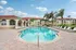 Elegant apartment community featuring a sparkling pool, surrounded by palm trees and stylish lounge chairs, against a backdrop of charming multi-story buildings.