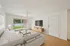 Bright and inviting living room with modern decor, featuring a cozy beige sofa, sleek wooden TV console, and expansive sliding glass doors opening to a lush green view.