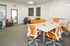 Bright and inviting social center with modern orange chairs, a sleek white table, and cozy gray armchairs, ideal for productive meetings.
