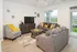 Inviting living room with modern gray furniture, accentuated by cheerful yellow pillows and decor. Large windows reveal a peaceful outdoor view, creating a bright and airy atmosphere.