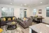 Modern living and dining area with stylish gray sofas, vibrant yellow accents, and a cozy round coffee table. Bright, airy space with large windows and a granite kitchen counter.