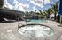 Luxurious outdoor pool area with a sunlit jacuzzi, surrounded by palm trees and elegant lounge chairs, perfect for relaxation and leisure.
