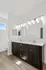 Contemporary bathroom with a sleek double vanity, elegant lighting, and large mirrors, featuring modern wood flooring and a window inviting natural light.