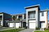 Modern townhouse with sleek architecture, bright facade, and elegant balconies, set against a vibrant blue sky and lush landscaping.