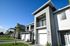 Modern townhouse with sleek design, large balcony, and manicured landscape, set against a vibrant blue sky.