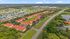 Aerial view of a vibrant residential community featuring charming red-roofed townhouses, lush green landscapes, and serene water bodies, offering a peaceful suburban lifestyle.