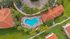 Aerial view of a luxurious residential complex with a beautifully landscaped pool area, surrounded by lush greenery and elegant red-roofed buildings, offering a tropical paradise feel.