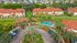 Vibrant aerial view of a charming apartment complex featuring stylish terracotta roofs, lush landscaped gardens, and a sparkling blue pool surrounded by palm trees.