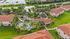 Scenic aerial view of a tropical apartment complex with terracotta roofs, lush landscaping, and an inviting pool area surrounded by palm trees.