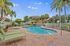 Inviting pool area surrounded by tropical palm trees and lush greenery, offering relaxing lounge chairs under a bright blue sky.