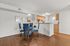 Elegant dining area with blue chairs, glass table, and modern kitchen, set on beautiful hardwood floors.