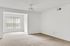 Spacious living area with soft beige carpet, large window for natural light, and a modern ceiling fan.