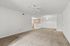 Bright living area with plush carpet and ceiling fan, flowing into a cozy kitchen with modern lighting and ample storage.