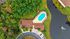Aerial view of a luxurious property featuring a sparkling pool with red sun loungers surrounded by lush greenery, adjacent to a serene lake and elegant buildings.
