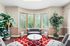Elegant living space with lush greenery, a plush gray sofa, and a vibrant red patterned rug, offering a cozy atmosphere.