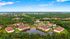 Stunning aerial view of a serene apartment community surrounded by lush greenery, featuring contemporary buildings with terracotta roofs and a reflecting pond, offering a tranquil living environment.