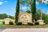 Charming entrance to Bella Vista Apartments, surrounded by lush greenery and elegant landscaping under a bright blue sky.