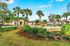 Charming apartment complex entrance with lush landscaping, palm trees, and a decorative fountain under a bright blue sky.