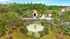 Charming villa entrance with lush landscaping and a central fountain surrounded by palm trees.