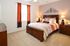 Warm and inviting bedroom with elegant wooden furniture, plush bedding, and vibrant orange curtains complementing the cozy ambiance.