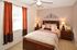 Cozy bedroom with elegant decor, featuring a plush bed, stylish bedside lamps, and warm natural light through red curtains.