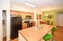 Inviting open-plan kitchen with sleek black appliances, stylish wooden cabinetry, and vibrant green bar stools, seamlessly flowing into a cozy dining area with lush decor.