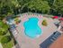 Inviting outdoor pool area featuring a sparkling blue pool surrounded by loungers, lush greenery, and vibrant red umbrellas, perfect for relaxation and entertainment.