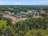 Aerial view of a picturesque apartment complex surrounded by lush greenery and expansive forests, featuring charming red-roofed buildings and ample parking.