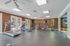 Bright and spacious gym with modern equipment, including treadmills and ellipticals, overlooking a sunlit patio through large windows.