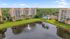 Serene lakeside apartment complex with lush green lawns, palm trees, and a sparkling blue pool, offering a tropical oasis vibe.
