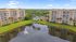 Elegant lakeside apartment complex with lush greenery, palm-dotted pool area, and tranquil fountain views.