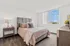 Bright and inviting bedroom featuring a plush bed with textured pink bedding, modern nightstand with a lamp, and a large window with scenic views.