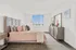 Bright and inviting bedroom featuring a plush bed with soft pink linens, elegant decor, and large window providing ample natural light.