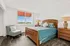 Bright and inviting bedroom with elegant wooden furniture, cozy bed with blue bedding, and a modern chair by a large window showcasing scenic views.