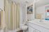 Bright and elegant bathroom featuring a clean white vanity, modern fixtures, and stylish striped shower curtain with floral wall art.