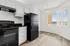 Bright modern kitchen with sleek black appliances, elegant white cabinetry, and large windows offering a scenic view.