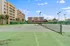 Spacious outdoor tennis courts with well-maintained netting, surrounded by modern apartment buildings and lush greenery, under a clear blue sky.