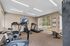 Bright apartment fitness room equipped with modern exercise bike, treadmill, and wall-mounted TV, offering a perfect workout space with outdoor views.
