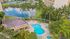 Luxurious apartment complex with a sparkling pool, surrounded by palm trees and overlooking a serene lake with tennis courts in the background.