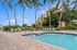 Inviting pool area with loungers and palm trees beside a modern apartment building under a clear blue sky.