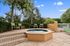 Inviting outdoor spa area with bubbling hot tub, surrounded by lush greenery and comfortable seating under a vibrant blue sky.