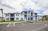 Modern apartment complex with sleek gray exterior, spacious balconies, and well-maintained landscaping under a bright blue sky.