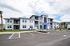 Modern apartment complex with sleek architecture, featuring large windows and spacious balconies, surrounded by lush landscaping under a bright sky.