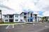 Modern three-story apartment building with sleek architecture, surrounded by landscaped greenery and ample parking space.