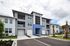 Modern three-story apartment building with sleek gray facade, blue accent, and lush landscaping in a vibrant community.