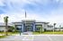 Modern office building with blue accents, surrounded by lush greenery and palm trees, located under a clear sky.