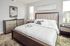 Elegant bedroom showcasing a plush bed with stylish cushions, modern dresser, and tasteful artwork in a serene, well-lit space.