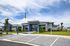 Modern community building with sleek design, featuring a grand entrance, blue accents, and lush landscaping under a vibrant sky.
