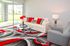 Bright and modern living room featuring a sleek white sofa with bold red and gray accents, set against a large glass balcony door offering scenic outdoor views.